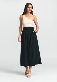 Čierna maxi sukňa s naťahovacím elastickým pásom, kombinovaná s béžovým rebrovaným topom na jedno rameno. Model má na sebe vrkôčikové sandále a minimalizované doplnky.