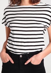 Stribet t-shirt i sort og hvid med en afslappet pasform, korte ærmer og en bred halsudskæring, kombineret med højtsiddende sorte bukser.