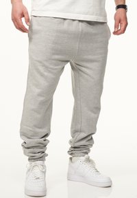 Graue Sweatpants aus weichem Stoff mit einer lockeren Passform, ausgestattet mit elastischen Bündchen und einem Kordelzugbund, kombiniert mit weißen Sneakers.