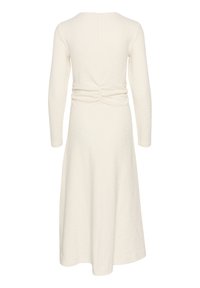 Långärmad klänning i krämfärg med texturerad tyg, som har en samlad detalj i ryggen och en utsvängd kjol. Bakvy visas.
