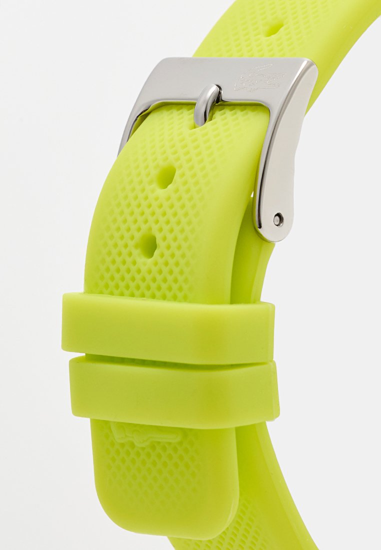 Neon żółty teksturowany pasek zegarka z silikonu z srebrną klamrą i dwoma uchwytami na pasek, zabezpieczony przez otwory do regulacji.