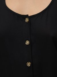 La blusa nera presenta un collo rotondo, quattro bottoni texture color marrone chiaro e un tessuto liscio con leggere arricciature sul colletto.