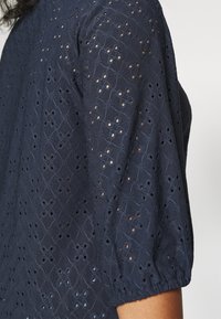 Navy blue eyelet blouse with puff sleeves, featuring a textured fabric and diamond stitching pattern with circular cutouts throughout.