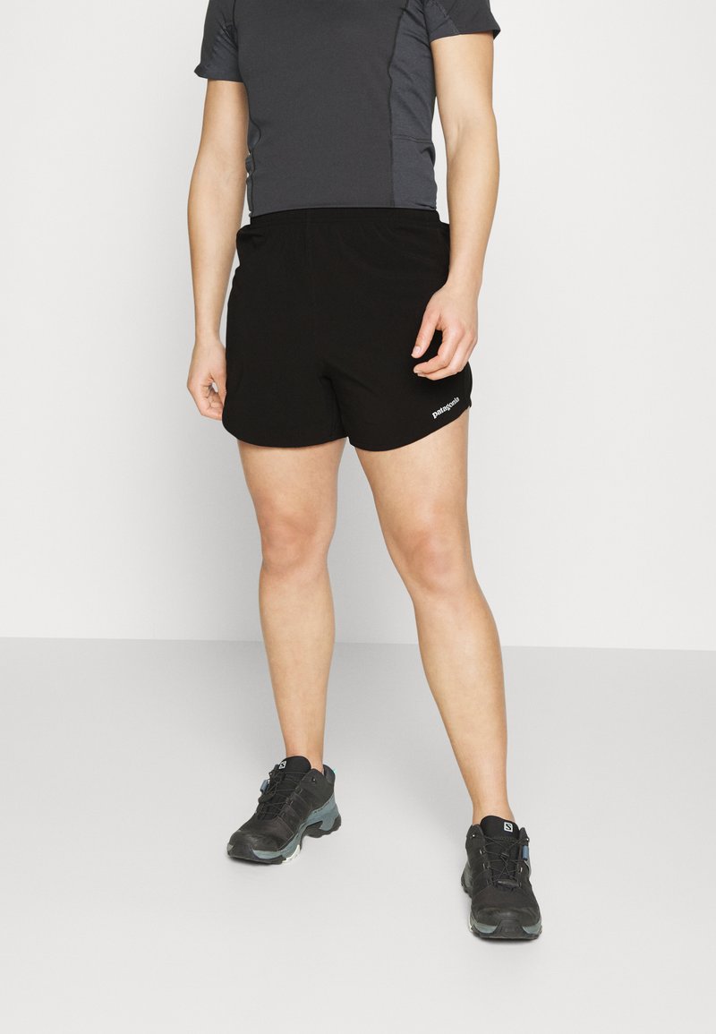 Calções desportivos pretos com um cós elástico, combinados com uma t-shirt de mangas curtas cinza escuro e sapatilhas de caminhada pretas. Design simples.