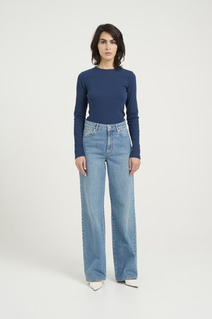 Navy ribbed long-sleeve top paired with high-waisted wide-leg light blue jeans. Model stands on a plain white background, with pointed white shoes.