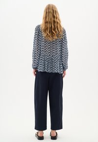Zračna bluza z modrim vzorcem in dolgimi rokavi, zasnovana s peplum detajli, kombinirana s prostornimi temno modrimi hlačami in črnimi sandali.