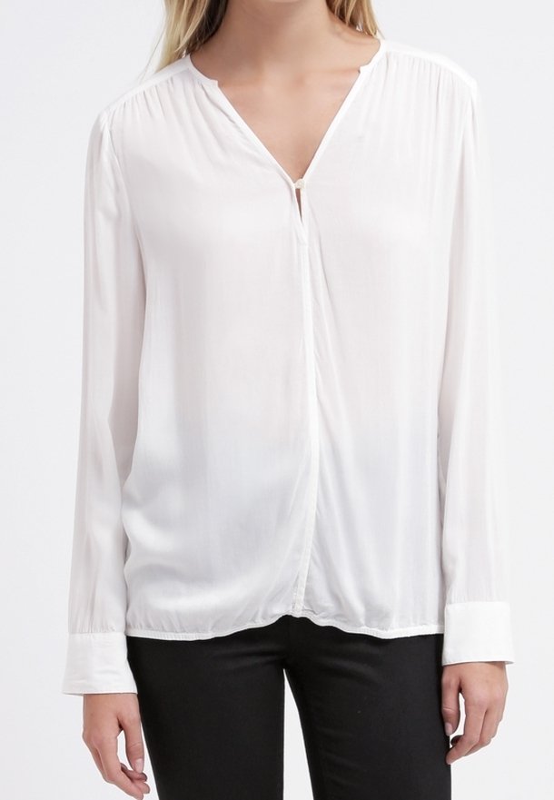 Blouse blanche à manches longues fabriquée en tissu léger avec un col en V, une patte de boutonnage à l'avant et des épaules froncées ; texture lisse et tomber doux.
