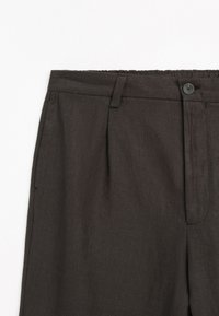 Pantaloni sartoriali grigio scuro con passanti per cintura, bottone frontale, tasche laterali e pieghe sottili su sfondo bianco.