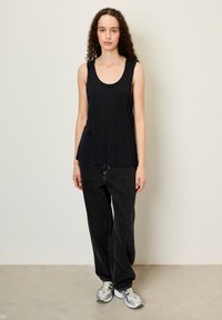 Juodas be rankovių marškinėlis su apvaliu iškirpimu, derinamas su plačiomis juodomis džinsinėmis kelnių ir pilkais sportbačiais su geltonais akcentais.