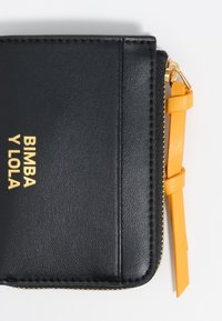 Czarny skórzany portfel z złotym logo "BIMBA Y LOLA", żółtym uchwytem do zamka błyskawicznego oraz teksturowanym wykończeniem. Zamek błyskawiczny zamykany wzdłuż jednej krawędzi.