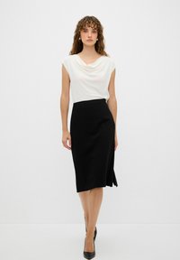 Bílá halenka s drapérií zkombinovaná s černou sukní délky ke kolenům, která má boční rozparek, elegantní design a hladkou texturu látky. Celkový vzhled doplňují černé lodičky.