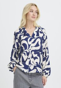 Langärmlige Bluse in Marineblau und Creme mit Muster, V-Ausschnitt, lässigem Schnitt und gesammelten Manschetten, aus strukturiertem Stoff gefertigt.