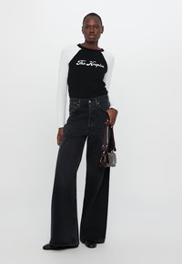 Black and white long-sleeve top with "The Kooples" text, paired with high-waisted black wide-leg jeans and a small burgundy handbag.
