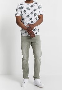 T-shirt blanc à manches courtes avec un motif floral vert, associé à un jean gris clair et des baskets blanches. Tenue simple et décontractée.