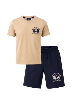 T-shirt beige a maniche corte e pantaloncini blu navy, entrambi con il logo del giocatore di polo La Martina sul petto sinistro e sulla gamba.
