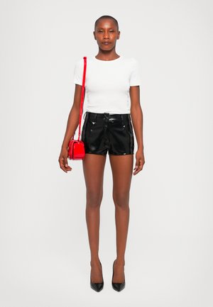 Black patent leather shorts, white fitted t-shirt, and red crossbody bag. Model wears black high heels. Plain background.