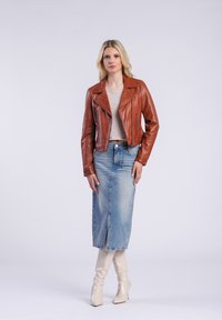 Bruine leren motorjack, grijs topje, blauwe denimrok met split en kniehoge witte laarzen. Eenvoudige achtergrond, neutrale kleuren.