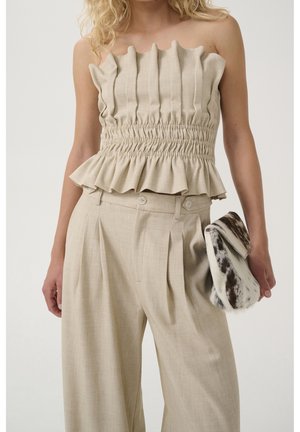 Woman wearing beige ruched strapless top and matching high-waisted wide-leg pants, holding a small black-and-white patterned clutch.