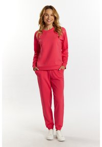 Różowa bluza i pasujące dresy wykonane z miękkiego materiału, z okrągłym dekoltem, ściągaczami przy mankietach i bocznymi kieszeniami. Białe sneakersy dopełniają całość.