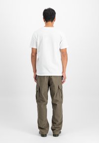 Baltas īsām piedurknēm T-krekls, kas kombinēts ar brīvi pieguļošiem olīvu zaļa krāsas kravas biksēm, kurām ir lielas sānu kabatas un relaksēts siluets.