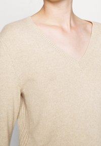 Ljusbeige v-neck-tröja med mjuk textur, ribbad halsringning och långa ärmar, med en avslappnad passform och minimal detaljering.