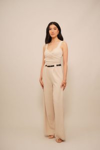 Combinaison beige avec un corps enroulé, jambes larges et une ceinture noire. Texture lisse, bretelles ajustables, légère plis sur le haut.