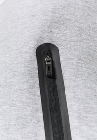 Tejido gris de textura suave con una cremallera negra vertical a lo largo del costado, que muestra un diseño elegante.