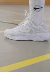 Baltie Nike sporta apavi ar sieta daļām, teksturētu vidusdaļu un gludu gumijas zoli. Valkāti ar baltiem zeķbiksēm.