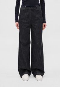 Tumši mazgātas, platām kājām džinsa bikses ar gludu tekstūru, augstu jostasvietu un slīpiem kabatām, kombinētas ar baltām sporta kurpēm.