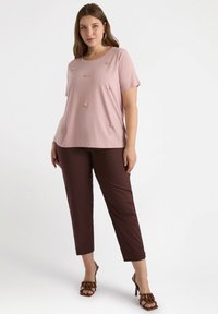 Camiseta de manga corta de color rosa claro con bordado floral en el frente, combinada con pantalones cortos marrones y sandalias de tacón marrones.