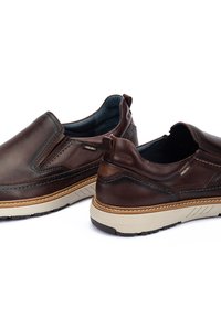 Zapatos marrones de piel extras suaves con un acabado texturizado, suela beige en contraste, paneles laterales elásticos y un interior suave. Logo de la marca visible.
