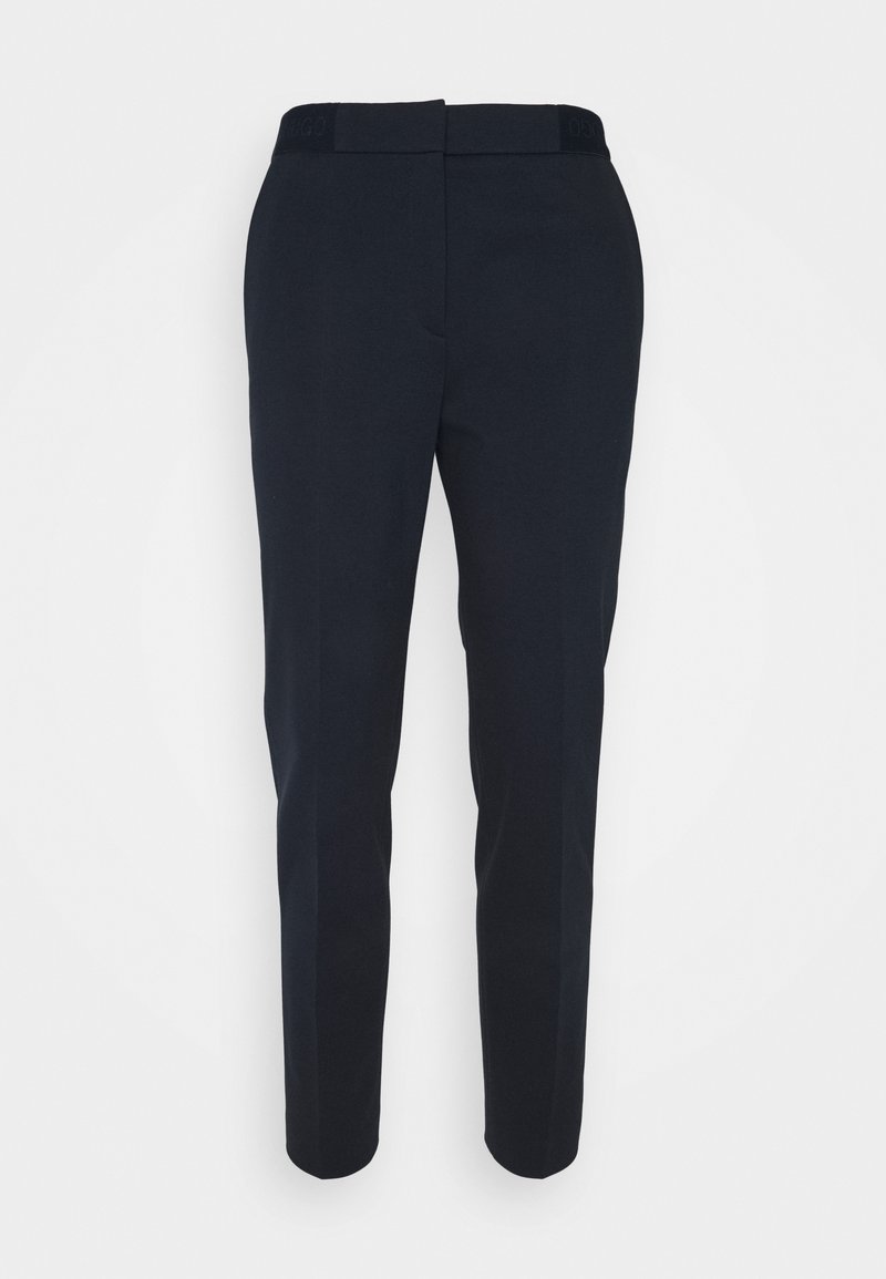 Pantalon bleu marine taillé sur mesure avec une coupe slim, présentant une texture lisse et une ceinture plate. Pas de poches visibles ni de motifs distincts.