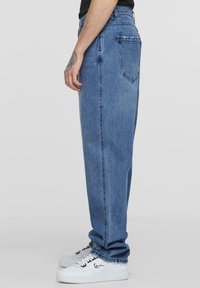 Jeans di denim azzurro chiaro con vestibilità dritta, vita alta e design a cinque tasche, abbinati a sneaker bianche con dettagli neri.