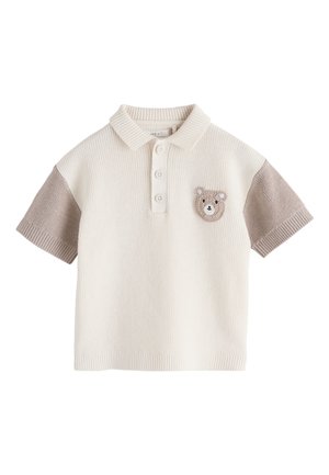 Polo corto de punto crema con mangas topo y un pequeño parche tejido con la cara de un oso en el pecho izquierdo.