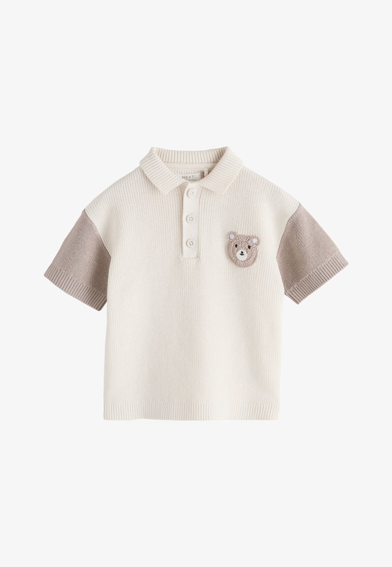 Polo court en maille crème avec manches taupe et petit écusson tricoté représentant un visage d'ours sur la poitrine gauche.