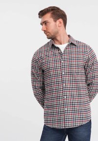 Camicia a maniche lunghe a quadri rossi, blu navy e bianchi, con chiusura a bottoni, colletto e taschino. Indossata con jeans blu.