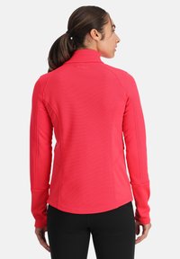 Fitted roze langemouwen jas met een geribbelde textuur, hoge kraag en naaddetails. Gladde stof loopt tot aan de taille, versierd met duimopeningen.