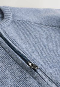 Fleece sweater in light blue, featuring a zip front with black metal hardware, ribbed neckline, and textured fabric.