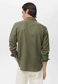 Camisa verde oliva de botones con un corte relajado, mangas largas y puños doblados, fabricada en un tejido texturizado con detalle de yugo en la espalda.