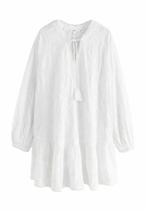 Blusa blanca bordada con escote en V y detalle de lazo, mangas largas abullonadas y dobladillo en capas. Recortes florales y textura ligera.