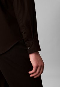 Black long-sleeve shirt with a buttoned cuff, smooth texture, tailored fit, and a subtle sheen, displayed against a light gray background.