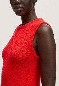 Rotes ärmelloses Stricktop mit strukturiertem Finish, rundem Ausschnitt und ungesäumten Kanten an den Armausschnitten. Weicher Stoff mit leicht lockerer Passform.