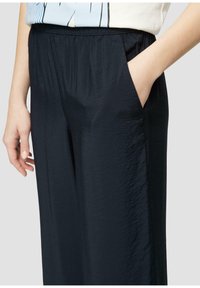 Černé, lehké kalhoty s elastickým pasem s hladkým povrchem a bočními kapsami. Design je volný pro pohodlí a snadnost pohybu.