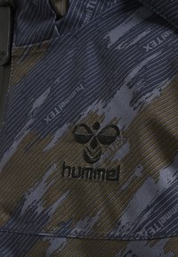 Navyblauer und goldfarbener Stoff mit einem auffälligen schwarzen gestickten Logo "hummel". Das Material wirkt leicht und hat eine strukturierte Oberfläche.