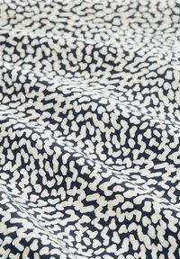 Baumwollstoff mit einem dunkelblauen Hintergrund und einem weißen abstrakten Muster. Die Textur wirkt glatt und leicht zerknittert.