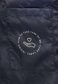 Marineblauem Stoff mit einer glatten Textur, der ein Pflegeetikett in einer Tasche aufweist, das eine Hand- und Herzgrafik mit Pflegehinweisen zeigt.