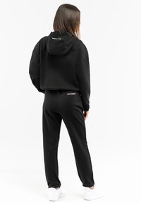 Black cropped hooded sweatshirt and matching pants in soft fabric, featuring "ICE ICEBERG" logo on the back and simple design.