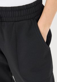 Svarta sweatpants med elastisk midja och sidfickor. Slät textur med avslappnad passform. Enkel design utan prydnader.