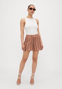 Body bianco senza maniche. Pantaloni corti multicolori a strisce con cintura elastica. Sandali con tacco a stiletto trasparenti. Occhiali da sole marroni.