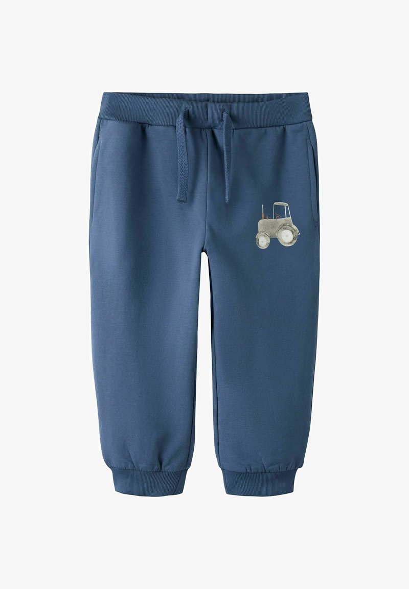 Pantaloni sport pentru copii mici, de culoare albastru, cu manșete cu dantelă, talie cu șnur, buzunare laterale și un mic desen gri cu un tractor pe partea dreaptă a coapsei.
